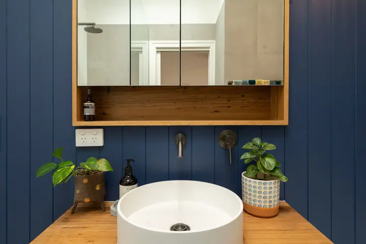 Round vessel basin on a timber vanity in front of a navy panelled wall